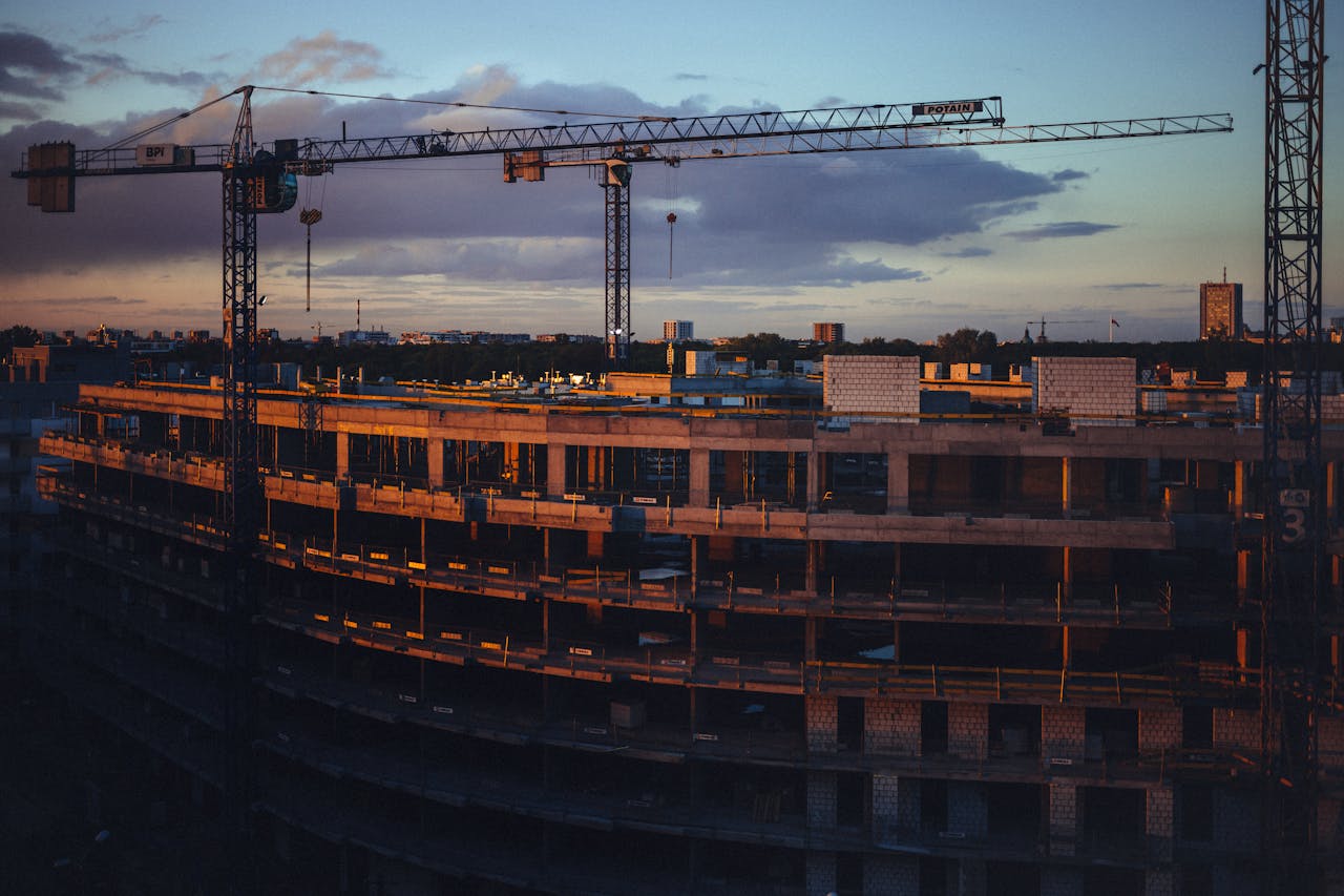 A construction site at sunset featuring cranes and a building under development.