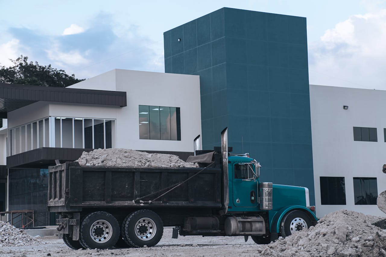 A dump truck loaded with materials parked near a modern building in Belize.